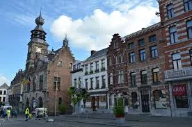 Débouchage Binche, devant l'hôtel de ville historique en pierre avec ses tours et fenêtres gothiques, rue animée par des passants