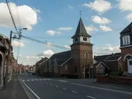 Plombier Oupeye dans une rue pittoresque avec maisons en briques rouges et végétation luxuriante typique de la région.